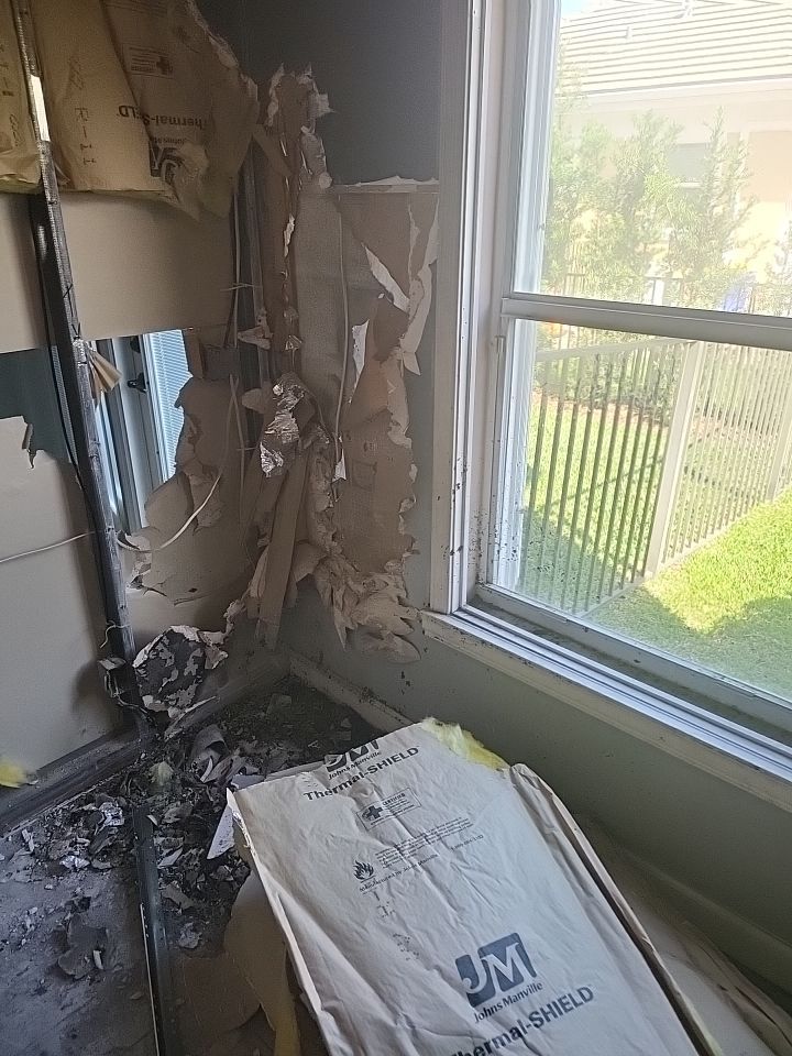 Fire damaged wall with torn drywall and insulation exposed near window